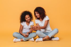 Brown skin woman and daughter both with curly hair in matching outfits of white shirt, blue jeans, and tennis shoes