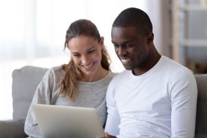 White woman with a grey long sleeve shirt and black man with a white long sleeve shirt looking at computer