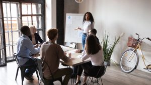 Brown skin woman with a white shirt and blue pants leading a business meeting