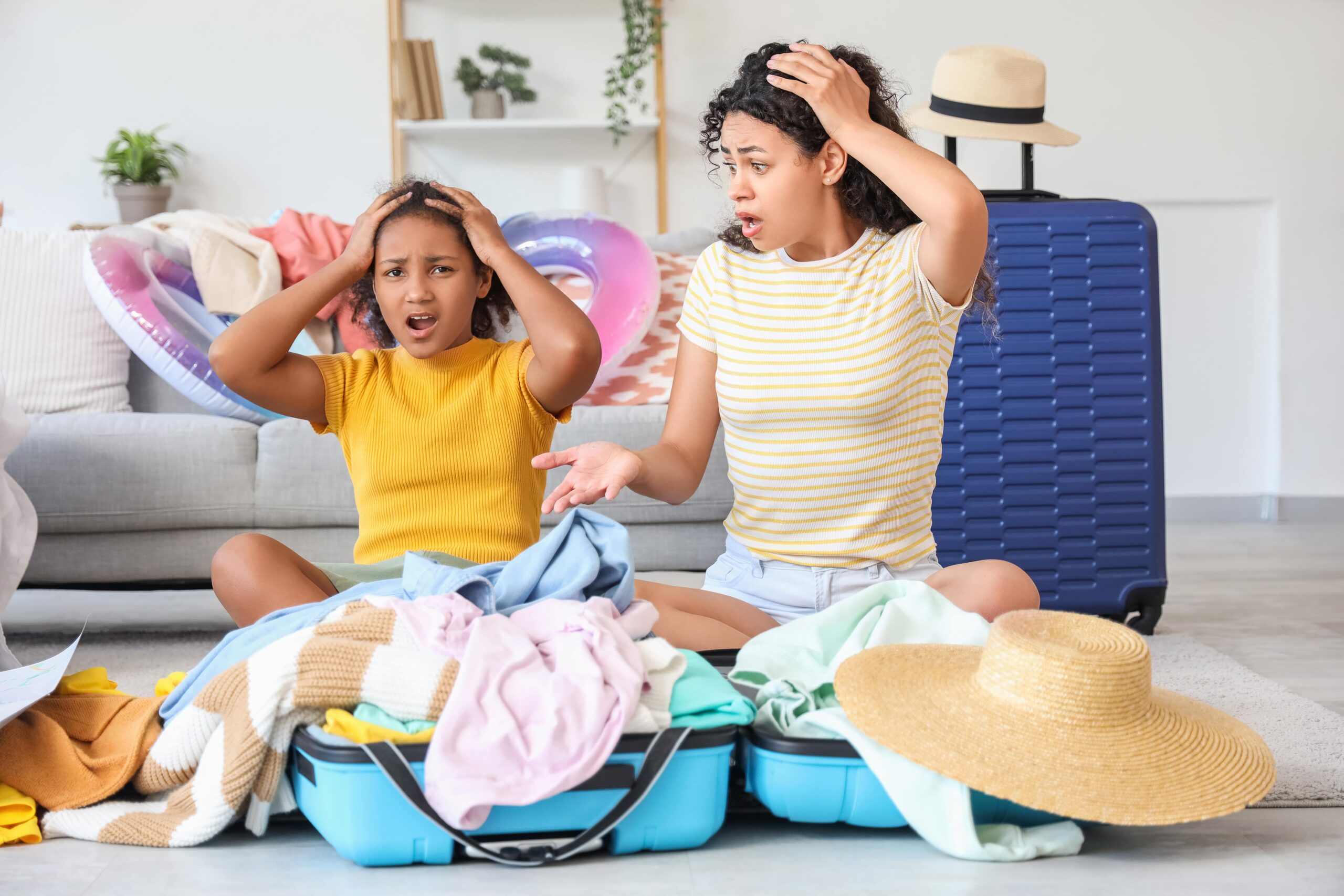 Mom with curly hair and bright shirt and Biracial daughter with yellow shirt with suitcase and clothes all over the floor