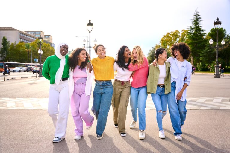Group of diverse confidently and happily women walking together with their arms behind each others backs, all wearing pants and their favorite colors